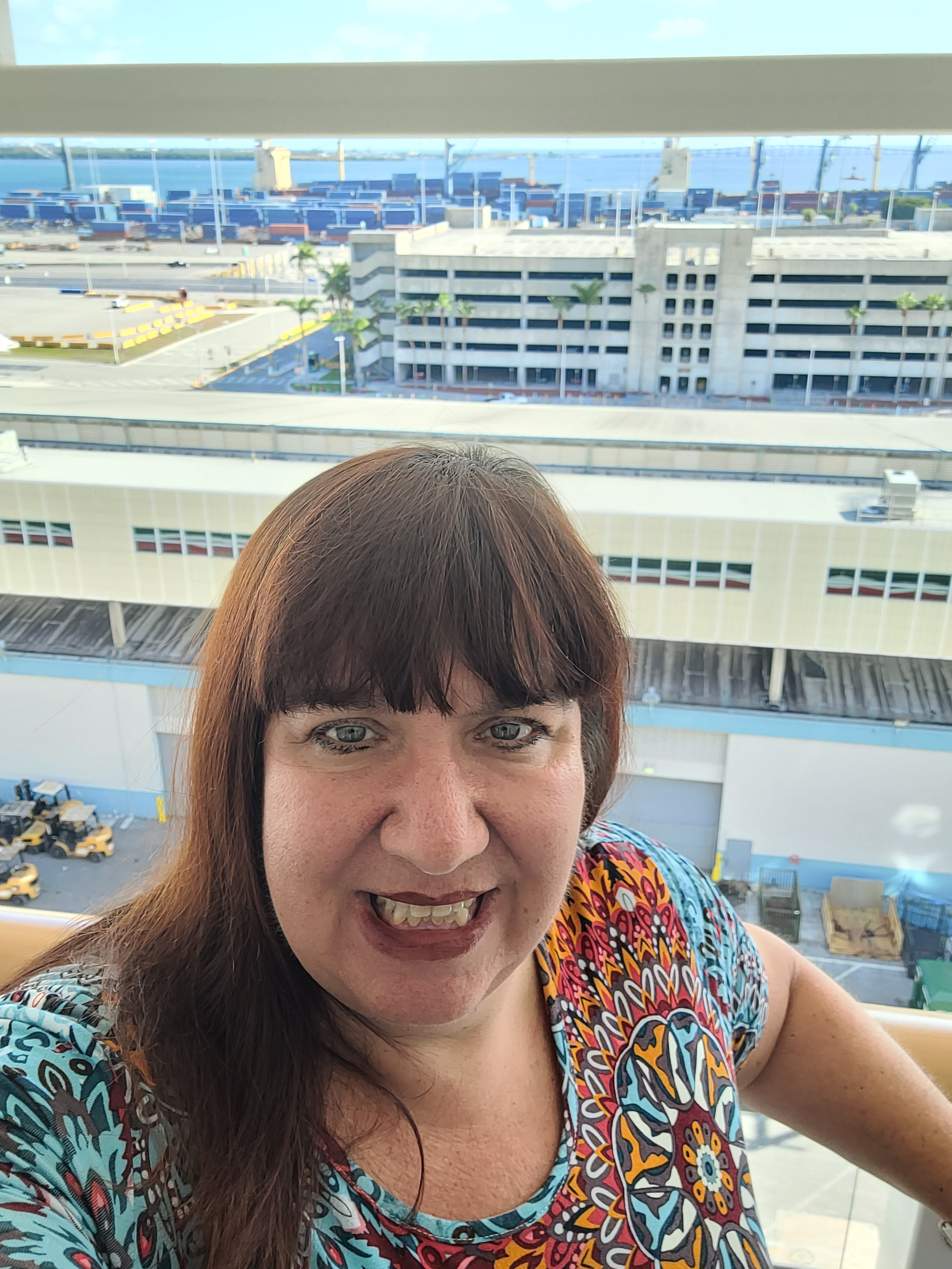 Jen Herold smiling on a cruise ship balcony with a port view behind her